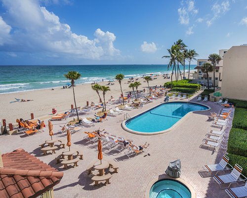 An outdoor swimming pool with a hot tub and chaise lounge chairs facing the beach.