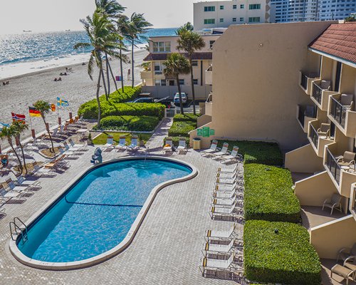 An outdoor swimming pool with chaise lounge chairs alongside resort units and the ocean.