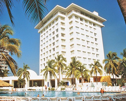 Exterior view of Hotel Emporio Ixtapa with an outdoor swimming pool chaise lounge chairs and palm trees.