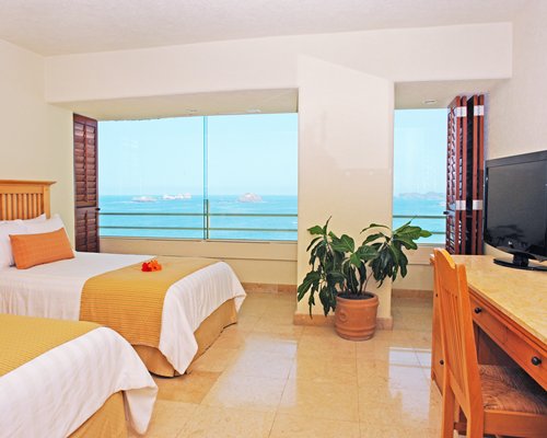 A well furnished bedroom with two multiple double beds television and an outside view.