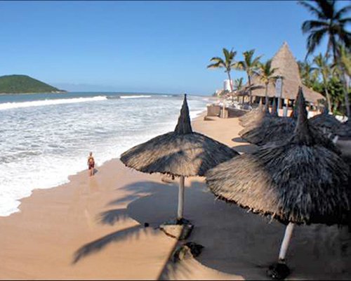 Beach view of thatched sunshades alongside the waterfront.
