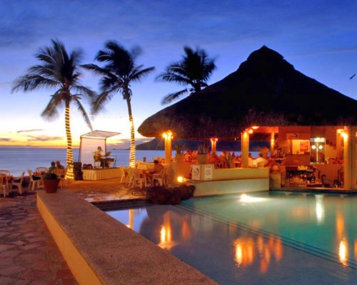 An outdoor swimming pool alongside the ocean at dusk.
