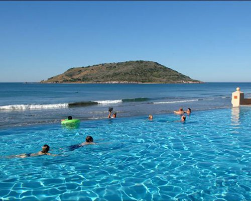 View of people at the outdoor swimming pool alongside the ocean.
