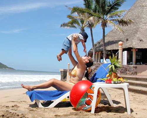 A woman playing with a kid in chaise lounge chair alongside the ocean.