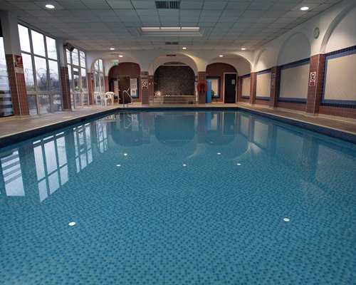Indoor swimming pool with patio chairs and outside view.