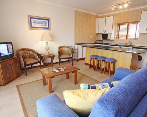 A well furnished living room with a television open plan kitchen and breakfast bar.