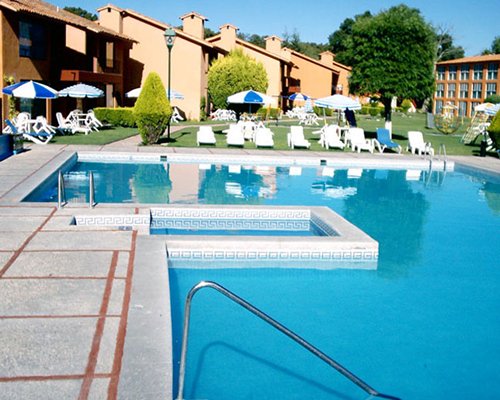 An outdoor swimming pool with sunshades and chaise lounge chairs alongside the resort.