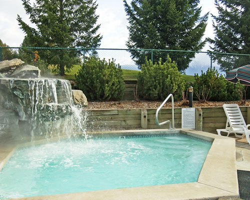 An outdoor swimming pool with water fountain chaise lounge chair and sunshade.