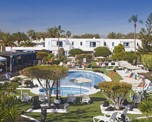 An outdoor swimming pool with hot tub and chaise lounge chairs sunshades.