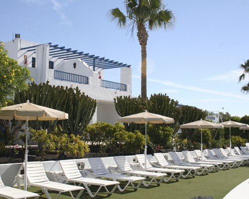An outdoor chaise lounge chairs with thatched sunshades alongside multi story resort units.
