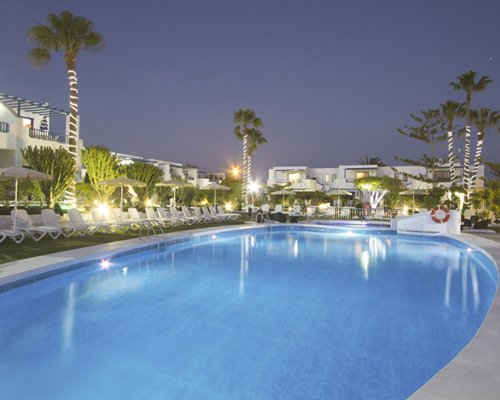 Night view of an outdoor swimming pool with chaise lounge chairs alongside the resort.