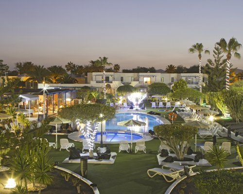 An outdoor swimming pool with hot tub and chaise lounge chairs sunshades at night.