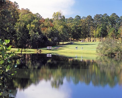 Golfers playing golf at the golf course alongside the lake surrounded by wooded area.