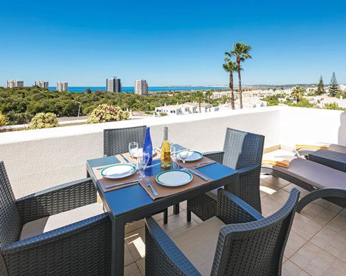 Balcony with outdoor dining area chaise lounge chairs and scenic landscape skyscrapers and ocean.