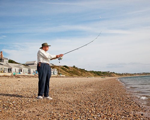 A man with a fishing rod at the beach alongside the resort.