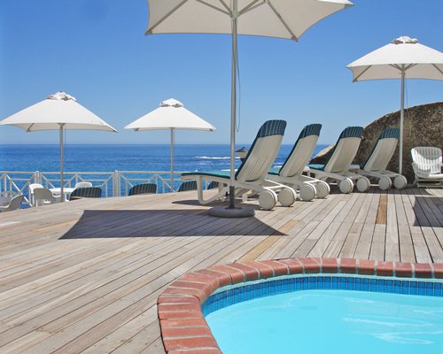 An outdoor swimming pool with chaise lounge chairs and umbrellas alongside the ocean.