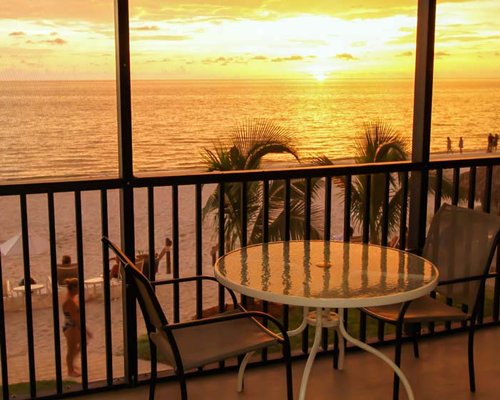 Balcony with patio furniture and view of the beach with palm trees.