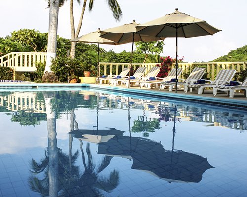 An outdoor swimming pool with chaise lounge chairs and thatched sunshades.