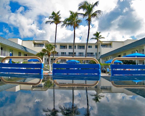 An exterior view of multi story resort units with chaise lounge chairs and thatched sunshades.