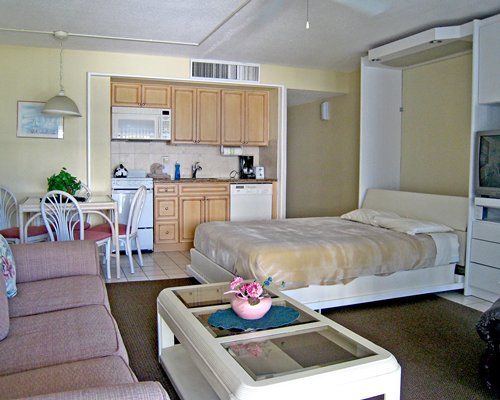 A well furnished living room with television dining area open plan kitchen and a bed.