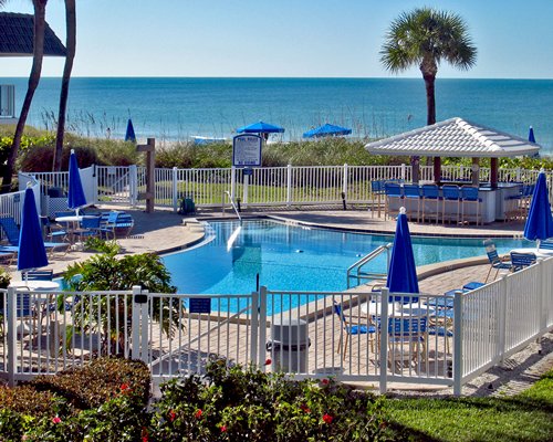 A scenic outdoor swimming pool with chaise lounge chairs and sunshades alongside the ocean.