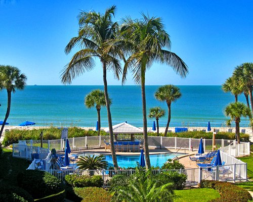 An outdoor swimming pool with sunshades and chaise lounge chairs alongside the ocean.