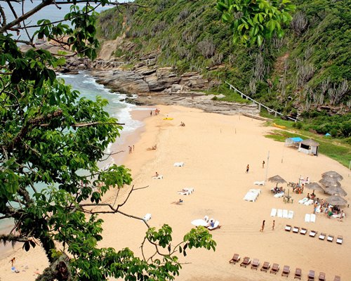 An aerial view of the beach with chaise lounge chairs and thatched sunshades alongside a mountain.