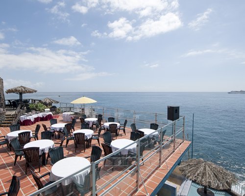 Outdoor restaurant with thatched sunshades alongside an ocean.