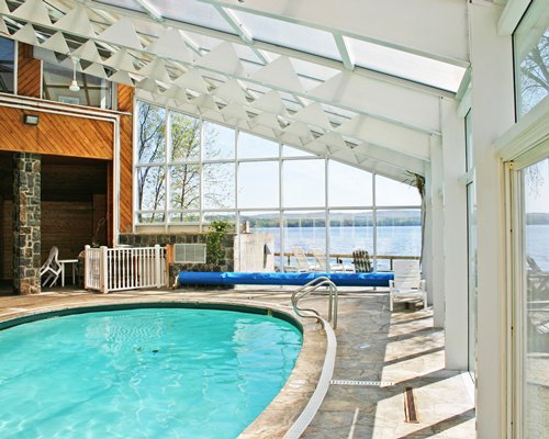 An indoor swimming pool with chaise lounge chairs and an outside view.