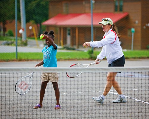 A woman teaching the tennis to a kid.