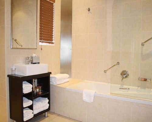 A bathroom with bathtub shower and a single sink vanity.