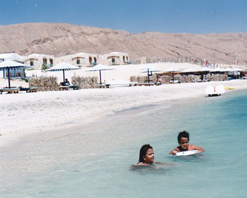 Kids swimming in the beach alongside resort units.