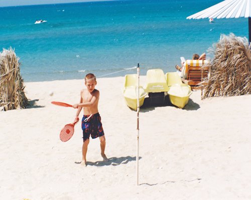 A kid playing badminton on the beach.
