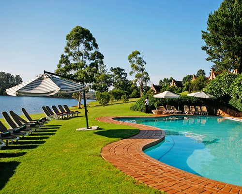 An outdoor swimming pool with chaise lounge chairs and sunshades alongside the lake.
