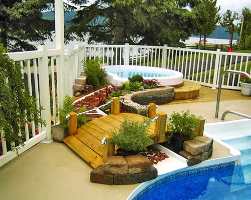 An outdoor swimming pool and hot tub alongside pine trees.