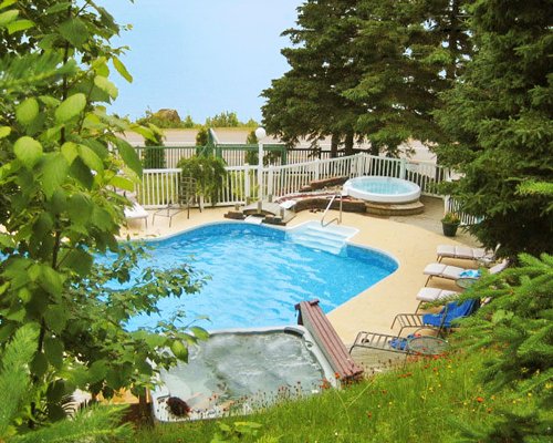 An outdoor swimming pool with hot tub and chaise lounge chairs surrounded by trees.