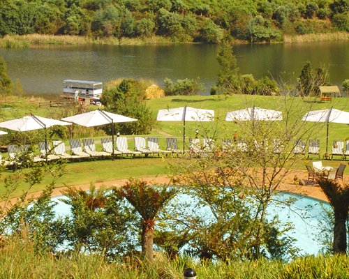 An outdoor swimming pool with chaise lounge chairs alongside the lake and wooded area.