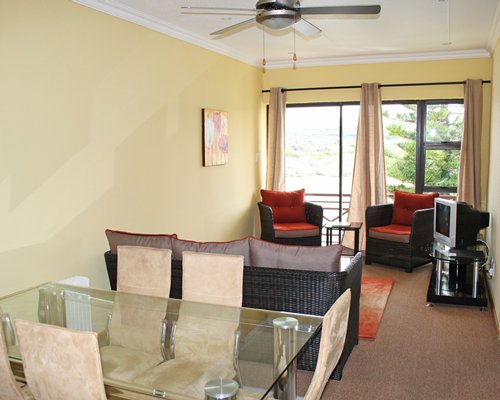 A well furnished living room with a television glass top dining area and outdoor view.