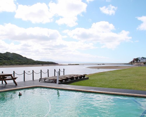 An outdoor swimming pool with chaise lounge chairs with the waterfront.