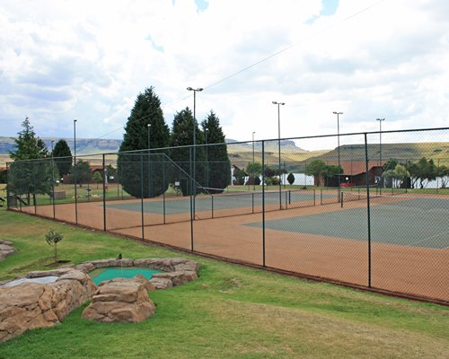 View of two outdoor tennis courts surrounded by trees.