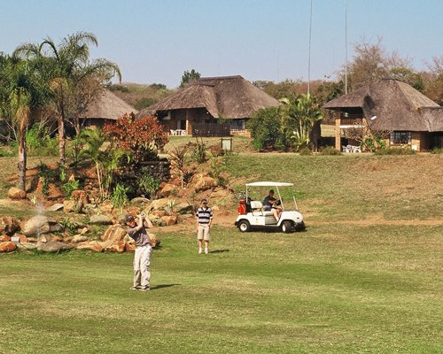 Two people playing in a well maintained golf course alongside golf cart.