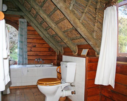 A bathroom with bathtub shower and single sink vanity with the thatched roof.