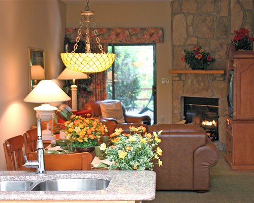 A well furnished living room with a television dining area fire in the fireplace double sink and patio.
