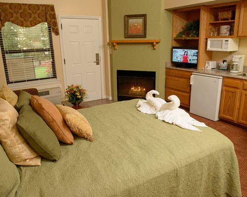 A well furnished bedroom with a king bed television open plan kitchen and fire in the fireplace.