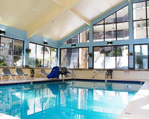 Indoor swimming pool with chaise lounge chairs patio furniture and outside view.