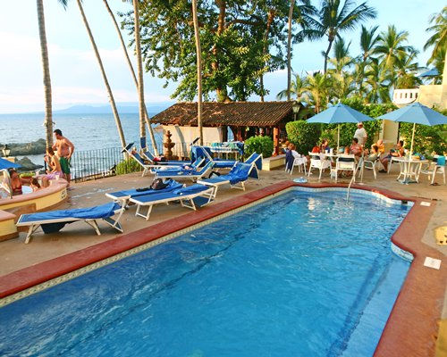 An outdoor swimming pool with hot tub chaise lounge chairs alongside the ocean.