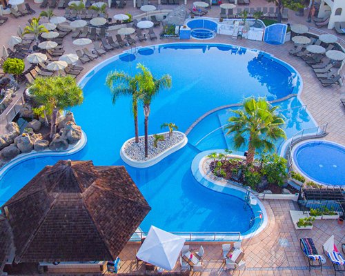 Large outdoor swimming pool with palm trees and sunshades alongside Royal Sunset Beach Club.