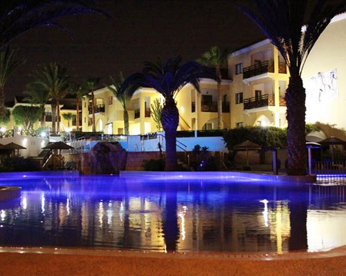 An outdoor swimming pool alongside multi story resort units at night.