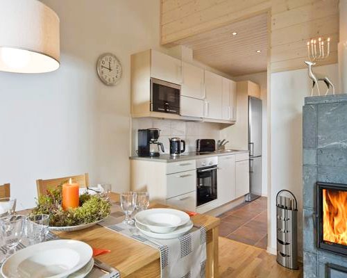 A wooden dining area alongside the kitchen and fire in the fireplace.