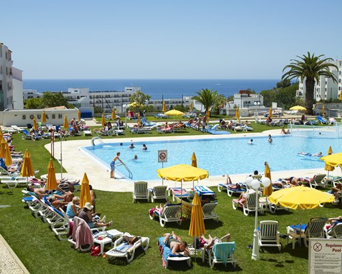 A scenic outdoor swimming pool with chaise lounge chairs and sunshades alongside the resort.